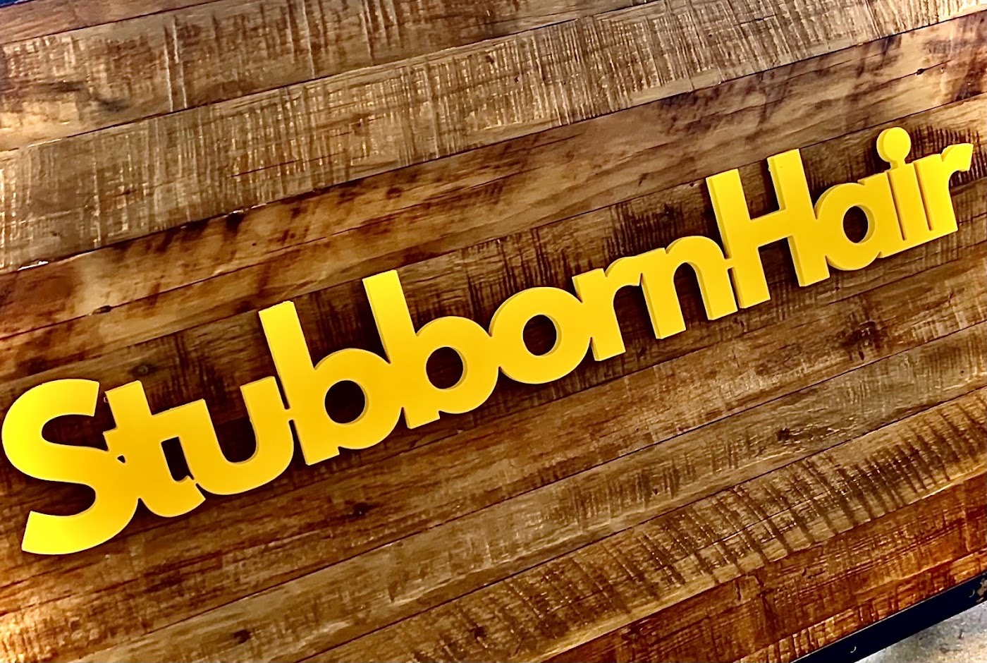 Yellow Stubborn Hair logo on reclaimed wood