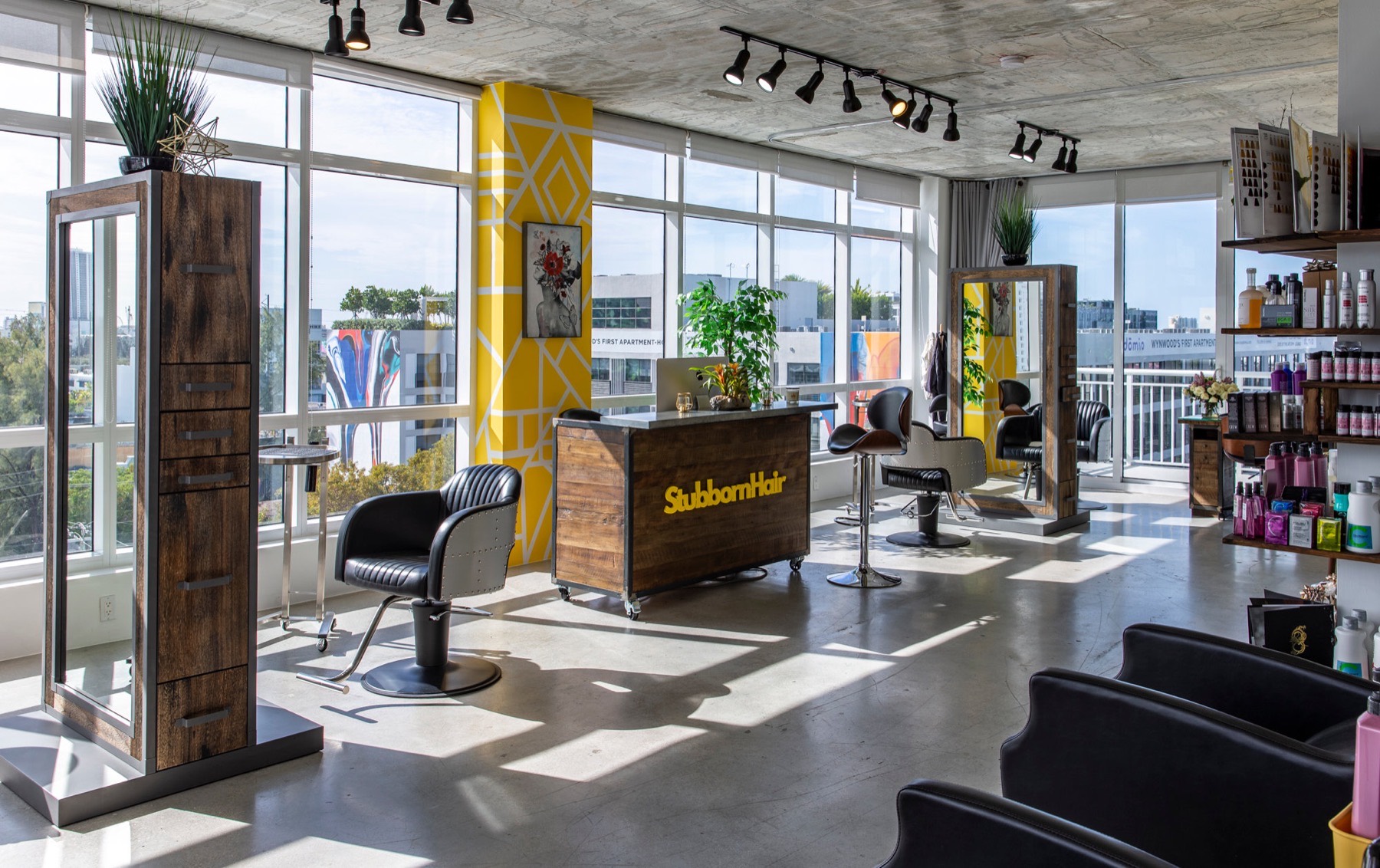 Sunlit Stubborn Hair studio with yellow geometric column, wooden reception desk and floor-to-ceiling windows